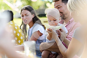 Cute baby eating honeydew at a summer garden party. The father is holding baby boy in his arms, mother feeding him.
