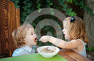 Cute baby food, babies eating. Little girl sister feeding baby. Good appetite.