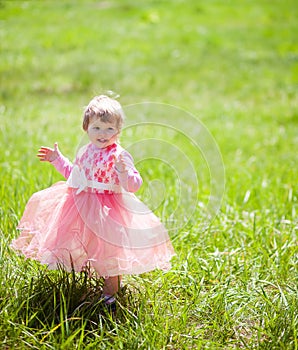 Cute baby girl 1-2 year old in fancy dress in the Park. Rejoice and clap their hands