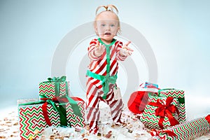 Cute baby girl 1 year old wearing santa hat posing over Christmas background. Sitting on floor with Christmas ball
