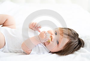 cute baby girl 6 month with nipple lying on a white bedding at home. top view.