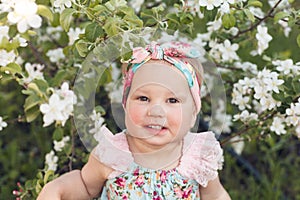 Cute baby girl on a background of white blossoms of an apple tree