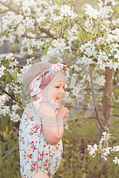 Cute baby girl on a background of white blossoms of an apple tree