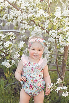 Cute baby girl on a background of white blossoms of an apple tree