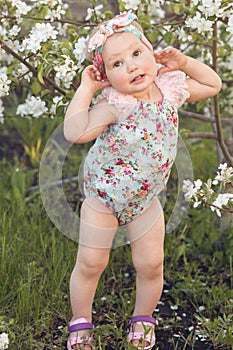 Cute baby girl on a background of white blossoms of an apple tree