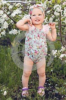 Cute baby girl on a background of white blossoms of an apple tree