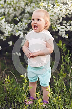 Cute baby girl on a background of white blossoms of an apple tree