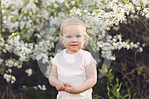 Cute baby girl on a background of white blossoms of an apple tree