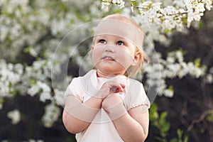 Cute baby girl on a background of white blossoms of an apple tree