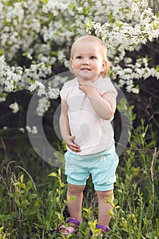 Cute baby girl on a background of white blossoms of an apple tree