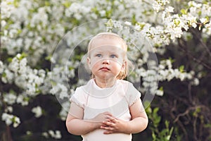 Cute baby girl on a background of white blossoms of an apple tree