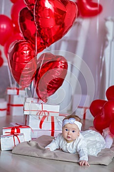 Cute baby girl celebrating birth day together close to red balloons.Lovely scene of baby on sofa divan with presents and