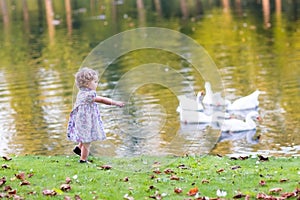 Cute baby girl chasing wild geese in an autumn park