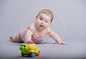 Cute baby girl crawling on the floor with colorful toy