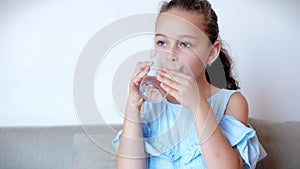 Cute baby girl drinking a glass of water sitting on the couch at home. Slow motion little boy drinking water. Close-up