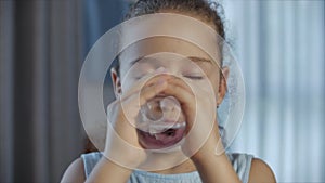 Cute baby girl drinking a glass of water sitting on the couch at home. Slow motion little boy drinking water. Close-up