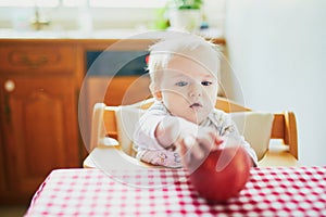 Cute baby girl eating apple in the kitchen