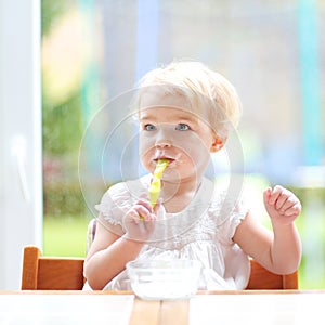 Cute baby girl eating yogurt from spoon