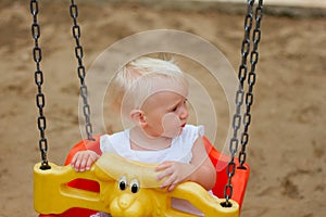 Cute blond baby girl sitting in a swing