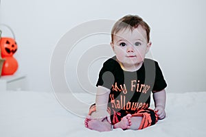 Cute baby girl in halloween costume at home, sitting on bed with Halloween decoration, Lifestyle indoors