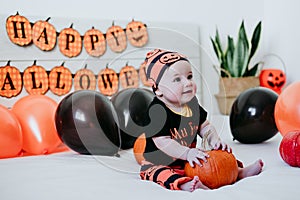 Cute baby girl in halloween costume at home, sitting on bed with Halloween decoration, Lifestyle indoors