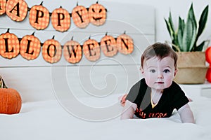 Cute baby girl in halloween costume at home, sitting on bed with Halloween decoration, Lifestyle indoors