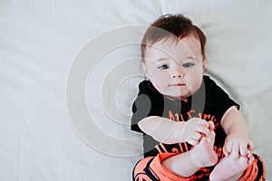 Cute baby girl in halloween costume at home, sitting on bed with Halloween decoration, Lifestyle indoors