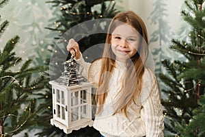 Cute baby girl holding a Christmas lantern among the Christmas trees.