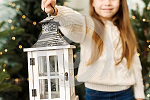 Cute baby girl holding a Christmas lantern among the Christmas trees.