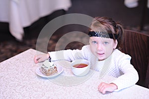 Cute baby girl holding cup of black tea in cafe