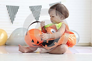 Cute baby girl kid dressing up in orange fancy Halloween pumpkin costume, cheerful little cute child holding orange pumpkin to