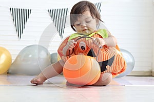 Cute baby girl kid dressing up in orange fancy Halloween pumpkin costume, cheerful little cute child holding orange pumpkin to