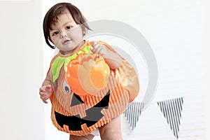 Cute baby girl kid dressing up in orange fancy Halloween pumpkin costume, cheerful little cute child holding orange pumpkin to