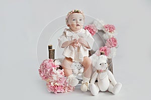 Cute baby girl in knitted clothes and wreath with teddy bear toy. Spring background with flowers. Children Protection Day. Mother