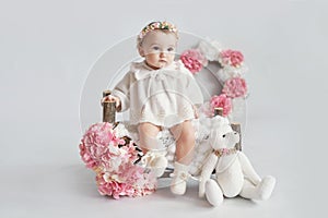 Cute baby girl in knitted clothes and wreath with teddy bear toy. Spring background with flowers. Children Protection Day. Mother