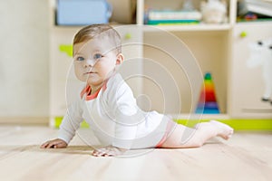 Cute baby girl learning crawling and sitting in children room at home. New born child, little girl lying on belly