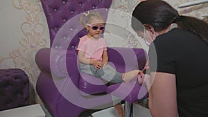 Cute baby girl at pedicure procedure in beauty spa salon.