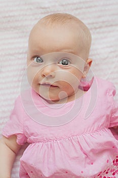 Cute baby girl in pink dress lies on white backgroun. Close-up portrait, cunning face.