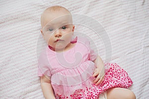 Cute baby girl in pink dress lies on white backgroun. Newborn child