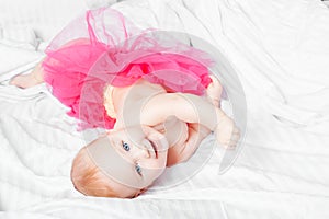 Cute baby girl in pink skirt with blue eyes over white blanket