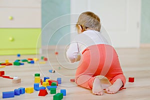 Cute baby girl playing with educational toys. Happy healthy child having fun with colorful different wooden blocks at