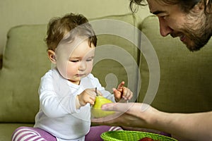 Cute baby girl plays with fruits with her father at home