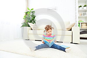 Cute baby girl reading book at home sitting on floor