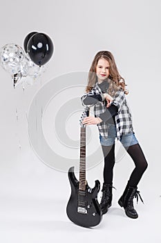 Cute baby girl rock star playing electric guitar and singing song surrounded by balloons