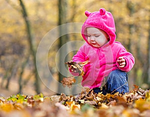 Cute baby girl sitting in autumn leaves