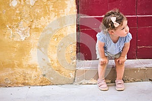 Cute baby girl sitting on the doorstep of a rural village home