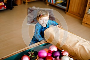 Cute baby girl taking down holiday decorations from Christmas tree. child holding light garland. Family after