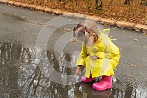 Cute baby girl toddler wearing yellow stylish raincoat pink rubber boots standing in a puddle