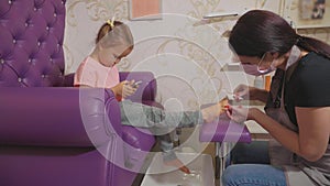 Cute baby girl using smart phone at pedicure procedure at beauty spa salon.