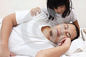 Cute baby girl wake her father up from sleep on the bed, morning hug and kiss from daughter